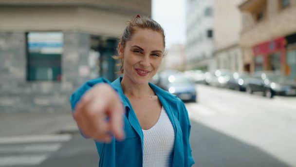 Young woman smiling confident pointing with finger at street - Foto, imagen