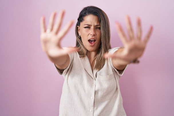 Mujer rubia de pie sobre fondo rosa haciendo stop gesture con las manos palmas, enojado y expresión de frustración  - Foto, Imagen