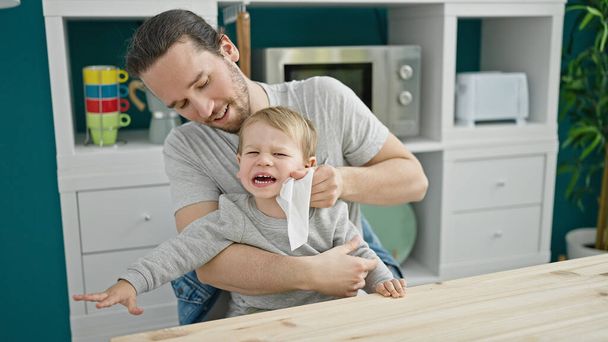 Isä ja poika istuvat pöydällä puhdistamassa kasvoja itkien ruokasalissa. - Valokuva, kuva