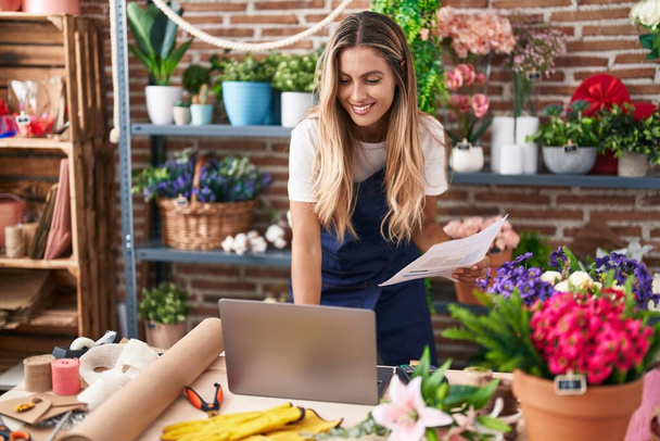 Young blonde woman florist using laptop reading document at florist - Photo, Image