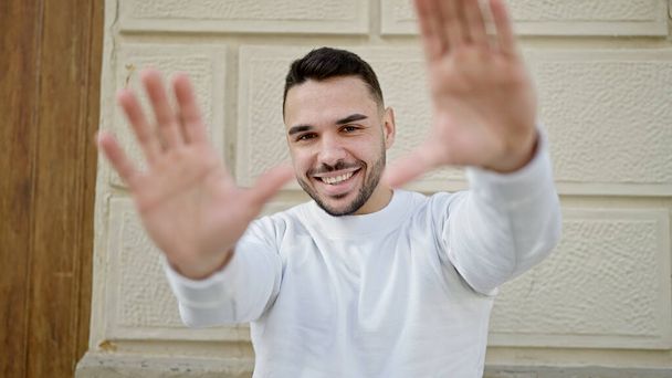 Молодой латиноамериканец, уверенно улыбающийся, делая подставной жест руками на улице - Фото, изображение