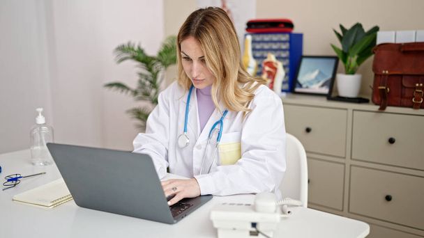 Νεαρή όμορφη ισπανίδα γιατρός χρησιμοποιώντας φορητό υπολογιστή που εργάζεται στην κλινική - Φωτογραφία, εικόνα
