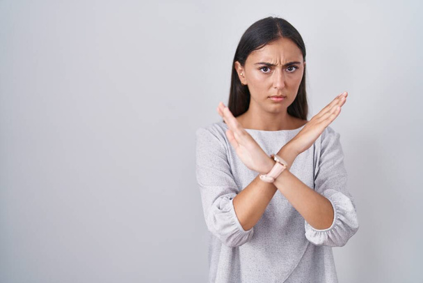 Young hispanic woman standing over white background rejection expression crossing arms doing negative sign, angry face  - Zdjęcie, obraz