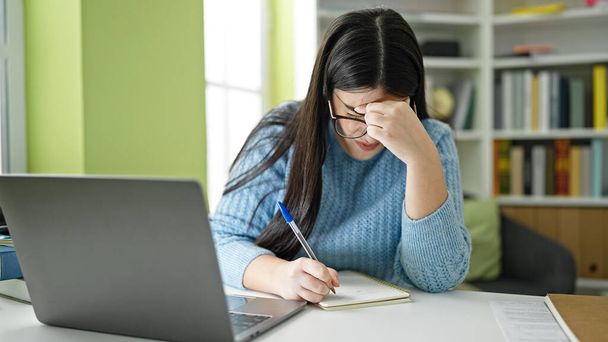 Genç İspanyol kız öğrenci dizüstü bilgisayar kullanmaktan ve kütüphanede not almaktan yoruldu. - Fotoğraf, Görsel
