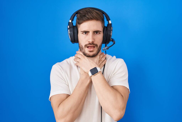 Hispanic man with beard listening to music wearing headphones shouting suffocate because painful strangle. health problem. asphyxiate and suicide concept.  - Foto, Imagen