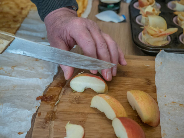 Ruce starého muže krájejí jablko na pečení dortu. Zavřít. Koncept stárnutí - Fotografie, Obrázek