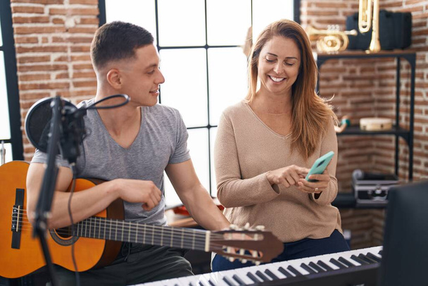 Man and woman musicians having classic guitar lesson using smartphone at music studio - Foto, Imagen