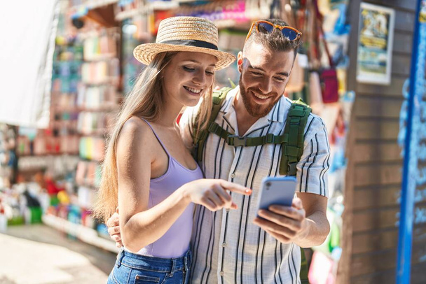 Hombre y mujer turista pareja sonriendo confiado usando teléfono inteligente en el mercado callejero - Foto, imagen