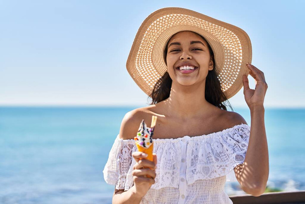 Young african american woman tourist smiling confident eating ice cream at seaside - Фото, изображение