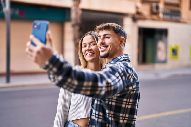 jong man en vrouw paar glimlachen zelfverzekerd maken selfie door de smartphone op straat - Foto, afbeelding