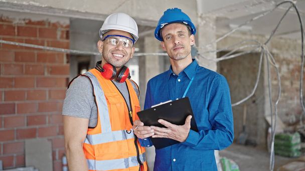 Два человека строитель и архитектор улыбается уверенно письменный документ на строительной площадке - Фото, изображение