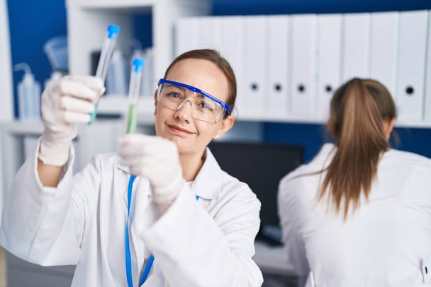 Zwei Wissenschaftlerinnen lächeln zuversichtlich und halten Reagenzgläser im Labor - Foto, Bild