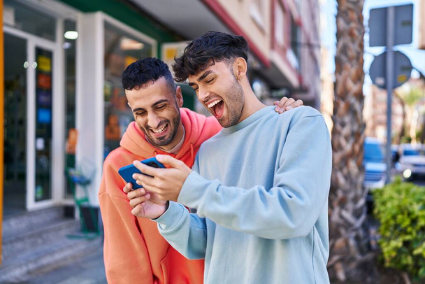 Twee man paar knuffelen elkaar met behulp van smartphone op straat - Foto, afbeelding