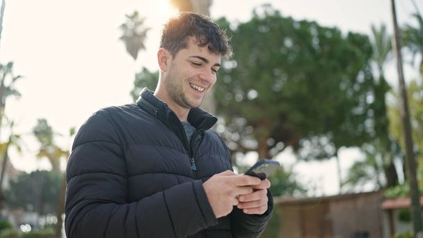 Nuori latino mies käyttää älypuhelin hymyilee puistossa - Valokuva, kuva