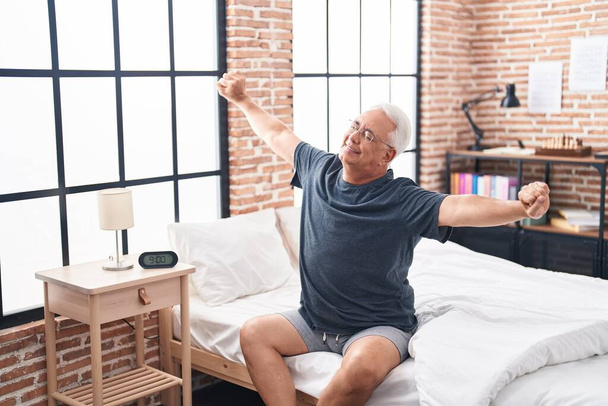 Middle age grey-haired man waking up stretching arms at bedroom - Fotografie, Obrázek