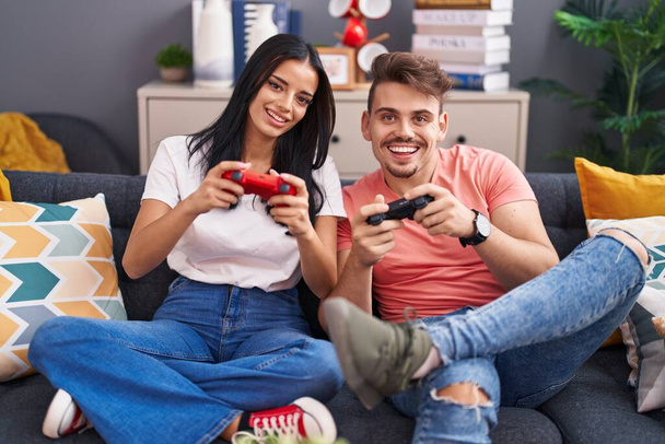Мужчина и женщина играют в видеоигры, сидя дома на диване - Фото, изображение