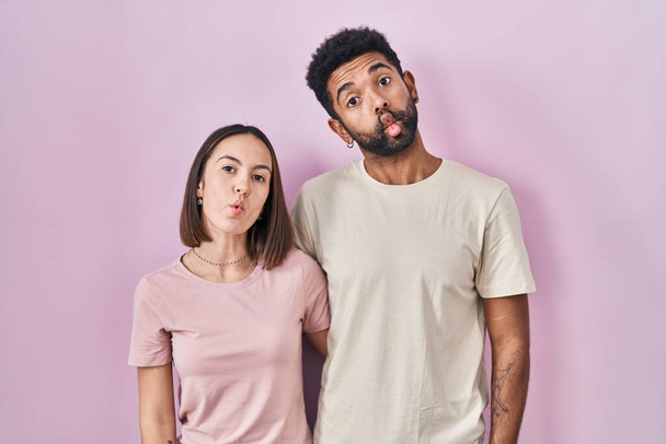 Fiatal spanyol pár együtt rózsaszín háttér, hogy hal arc ajkakkal, őrült és komikus gesztus. Vicces kifejezés..  - Fotó, kép