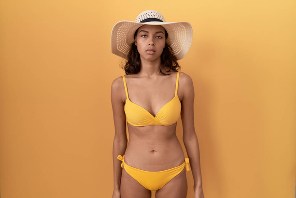 Young hispanic woman wearing bikini and summer hat looking sleepy and tired, exhausted for fatigue and hangover, lazy eyes in the morning.  - Photo, Image