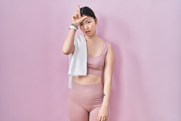 Chinese young woman wearing sportswear and towel making fun of people with fingers on forehead doing loser gesture mocking and insulting.  - Zdjęcie, obraz
