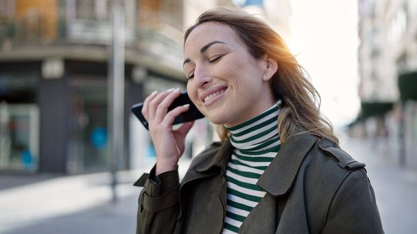 Mladý krásný hispánský žena usměvavý sebevědomý poslech audio zprávy s smartphone na ulici - Fotografie, Obrázek