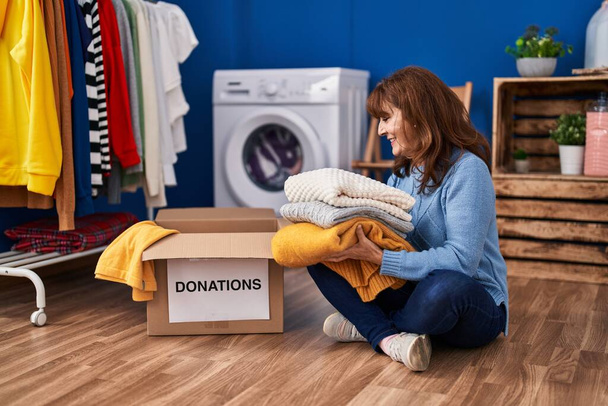 Middle age woman smiling confident donate clothes at laundry room - Фото, зображення