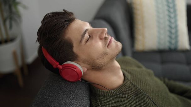 Young hispanic man listening to music relaxed on sofa at home - Photo, image