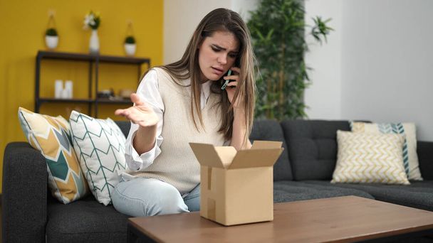 Молода красива іспаномовна жінка розмовляє по телефону розпаковуючи картонну коробку вдома
 - Фото, зображення