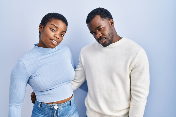 青の背景に立っている若いアフリカ系アメリカ人のカップルは、眠いと疲れて、疲労と格納庫のために疲れ、午前中に怠惰な目を見て.  - 写真・画像