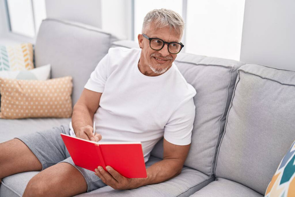 Libro di lettura uomo medioevo dai capelli grigi seduto sul divano di casa - Foto, immagini