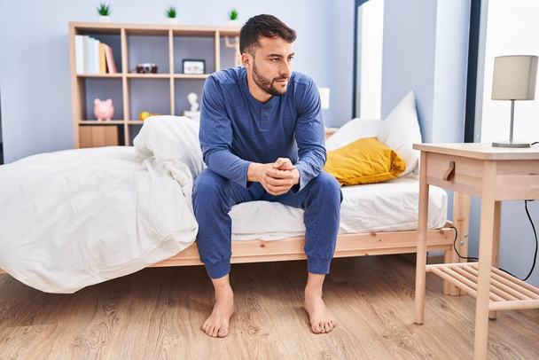 Young hispanic man sitting on bed at bedroom - Photo, Image