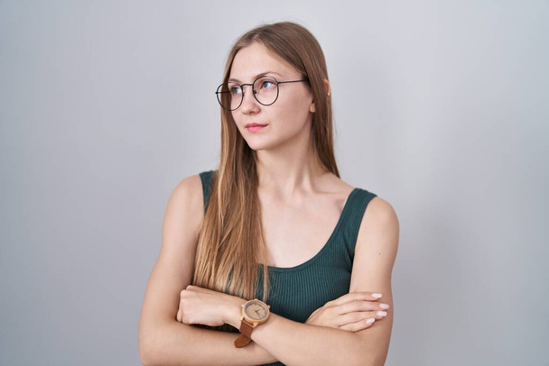 Young caucasian woman standing over white background looking to the side with arms crossed convinced and confident  - Fotografie, Obrázek