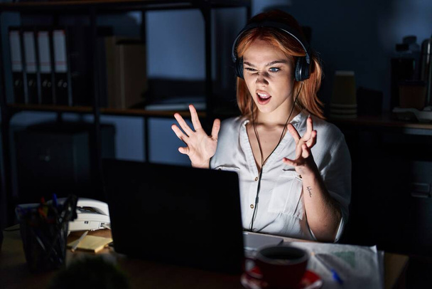 Young caucasian woman working at the office at night crazy and mad shouting and yelling with aggressive expression and arms raised. frustration concept.  - Fotoğraf, Görsel