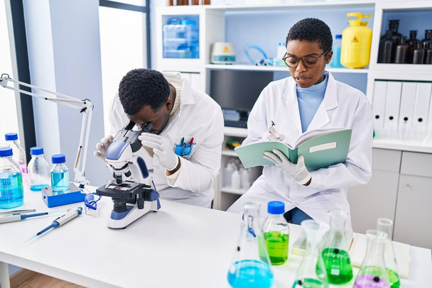 Άνδρες και γυναίκες επιστήμονες που χρησιμοποιούν μικροσκόπιο γραφής σε σημειωματάριο στο εργαστήριο - Φωτογραφία, εικόνα
