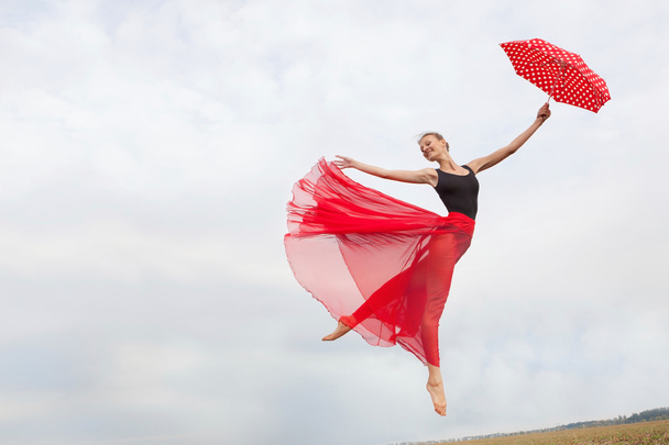 Молодая женщина, летающая в небе с красным зонтиком
 - Фото, изображение
