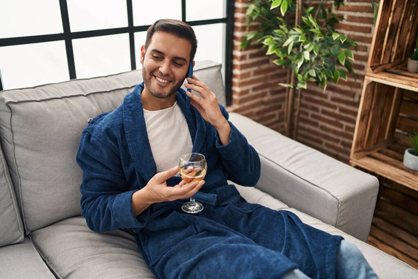 Young hispanic man talking on the smartphone and drinking wine at home - Φωτογραφία, εικόνα