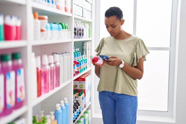 Cliente afroamericano usando un teléfono inteligente que sostiene el frasco de medicina en la farmacia - Foto, imagen