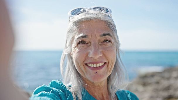 Mulher de cabelos grisalhos de meia idade turista fazendo selfie pela câmera na praia - Foto, Imagem