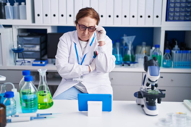 Senior woman scientist using touchpad with serious expression at laboratory - Photo, Image