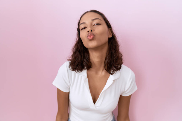 Mujer hispana joven vistiendo camiseta blanca casual mirando a la cámara soplando un beso en el aire siendo encantadora y sexy. expresión de amor.  - Foto, Imagen