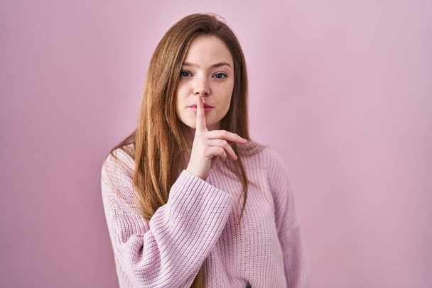 Young caucasian woman standing over pink background asking to be quiet with finger on lips. silence and secret concept.  - Fotografie, Obrázek
