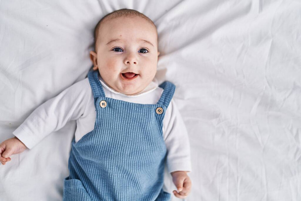Imádnivaló baba mosolyog magabiztos feküdt az ágyon a hálószobában - Fotó, kép