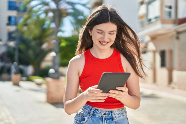 Νεαρή καυκάσια γυναίκα χαμογελά με αυτοπεποίθηση χρησιμοποιώντας touchpad στο πάρκο - Φωτογραφία, εικόνα