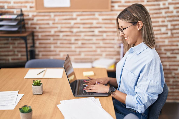 Genç, güzel İspanyol iş kadını ofisteki dizüstü bilgisayarını kullanarak gülümsüyor. - Fotoğraf, Görsel