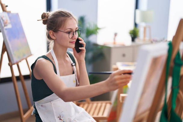 Young caucasian woman artist talking on smartphone drawing at art studio - Foto, immagini