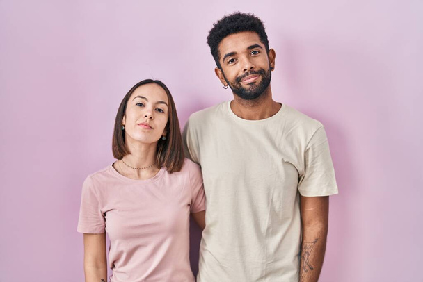 Νέοι Ισπανοί ζευγάρι μαζί πάνω από ροζ φόντο χαλαρό με σοβαρή έκφραση στο πρόσωπο. απλή και φυσική κοιτάζοντας την κάμερα.  - Φωτογραφία, εικόνα