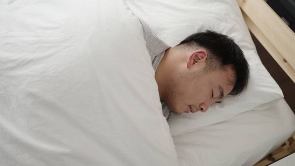 Young chinese man lying on bed sleeping at bedroom - Fotografie, Obrázek