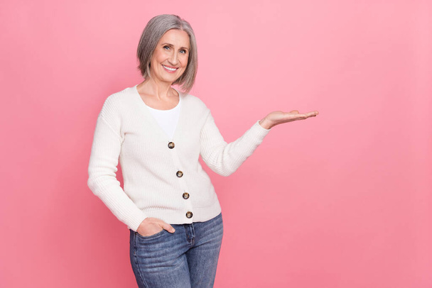 Photo of nice positive aged lady toothy smile arm palm hold demonstrate empty space isolated on pink color background. - Foto, afbeelding