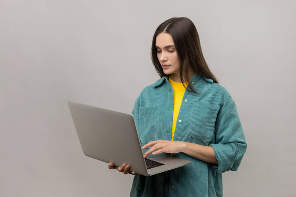 Portrait of smiling freelance worker woman holding laptop, using computer for education or online job, browsing internet, wearing casual style jacket. Indoor studio shot isolated on gray background. - Foto, Bild