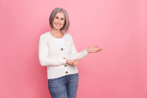 Photo of cheerful nice aged lady toothy smile arms demonstrate empty space offer proposition isolated on pink color background. - Foto, Imagem