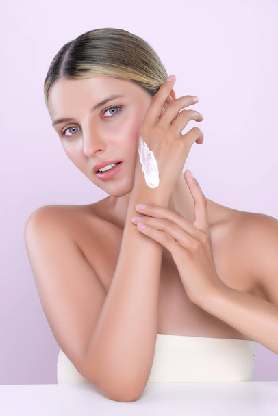 Intrygująca piękna kobieta stosująca krem nawilżający na rękę dla doskonałej pielęgnacji skóry w różowym odizolowanym tle. Białe kobiety portret z odmładzania skóry i koncepcji kosmetologii. - Zdjęcie, obraz